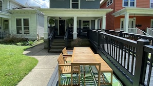 Une maison à deux étages dotée d’un porche abrité, d’une terrasse en bois et d’un escalier menant à l’étage supérieur.