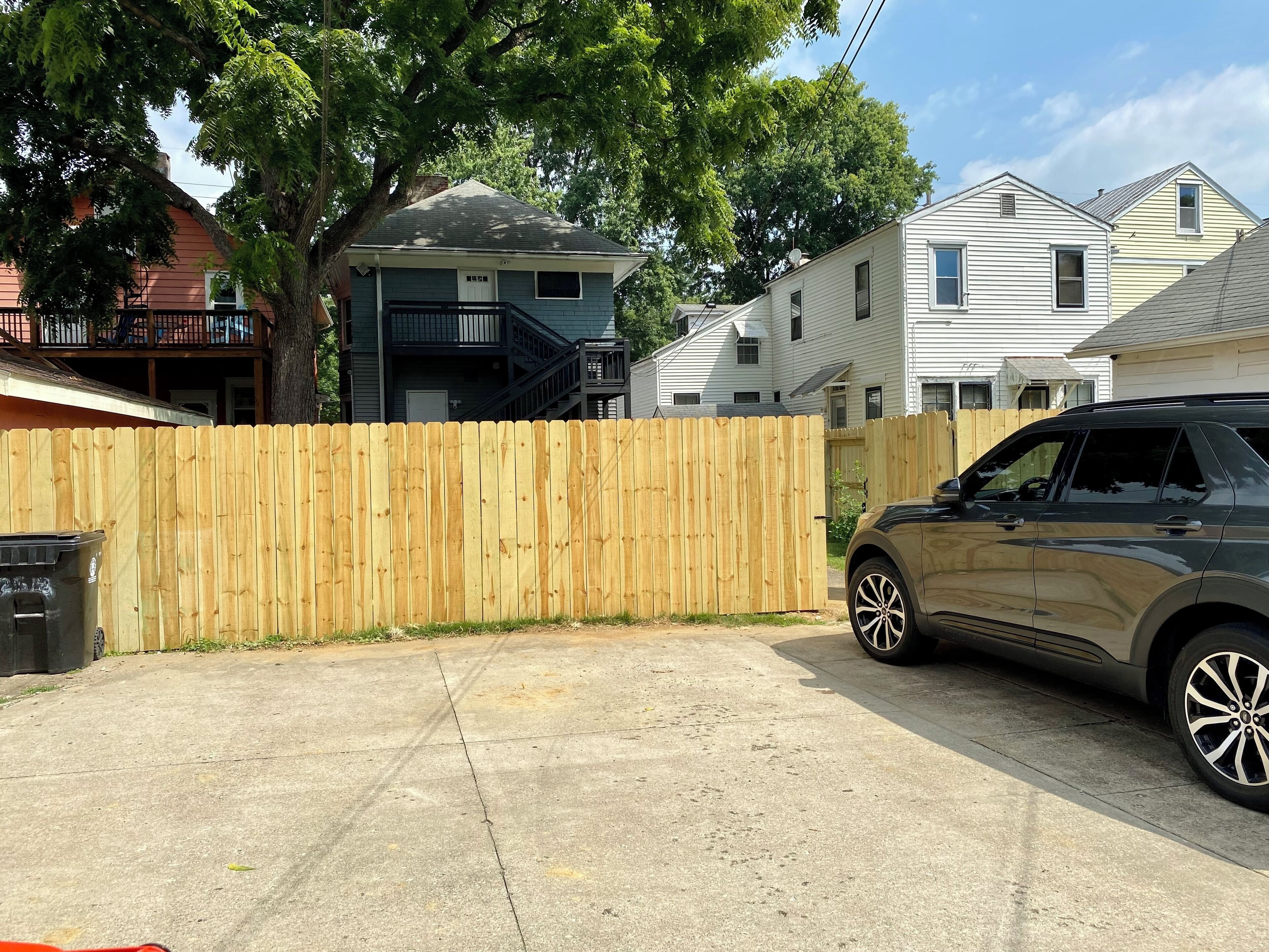 A residential area with a wooden fence, a parked car, and houses in the background.