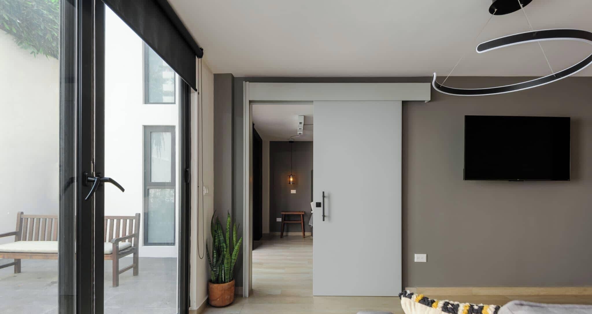 A modern interior with a large window, a flat-screen TV mounted on the wall, a wooden bench, and a potted plant.