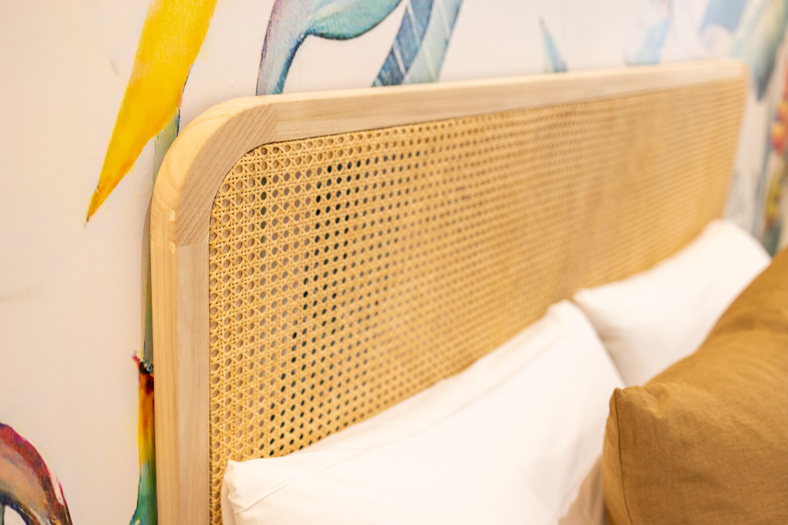 Un lit avec une tête de lit en osier, des oreillers blancs et un coussin marron.