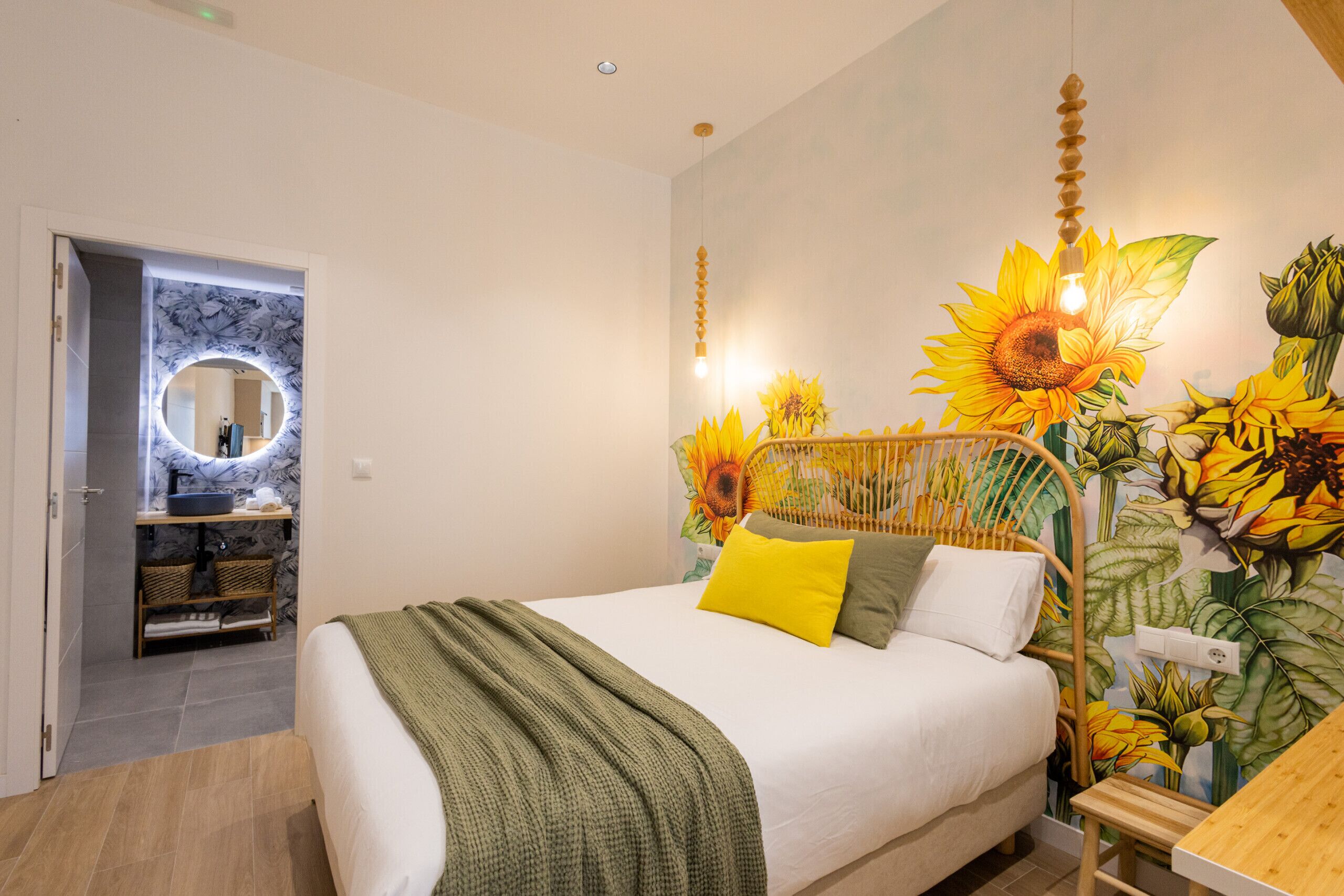 Une chambre à coucher avec un lit, une fresque murale représentant des tournesols, une tête de lit en bois et une petite table en bois.