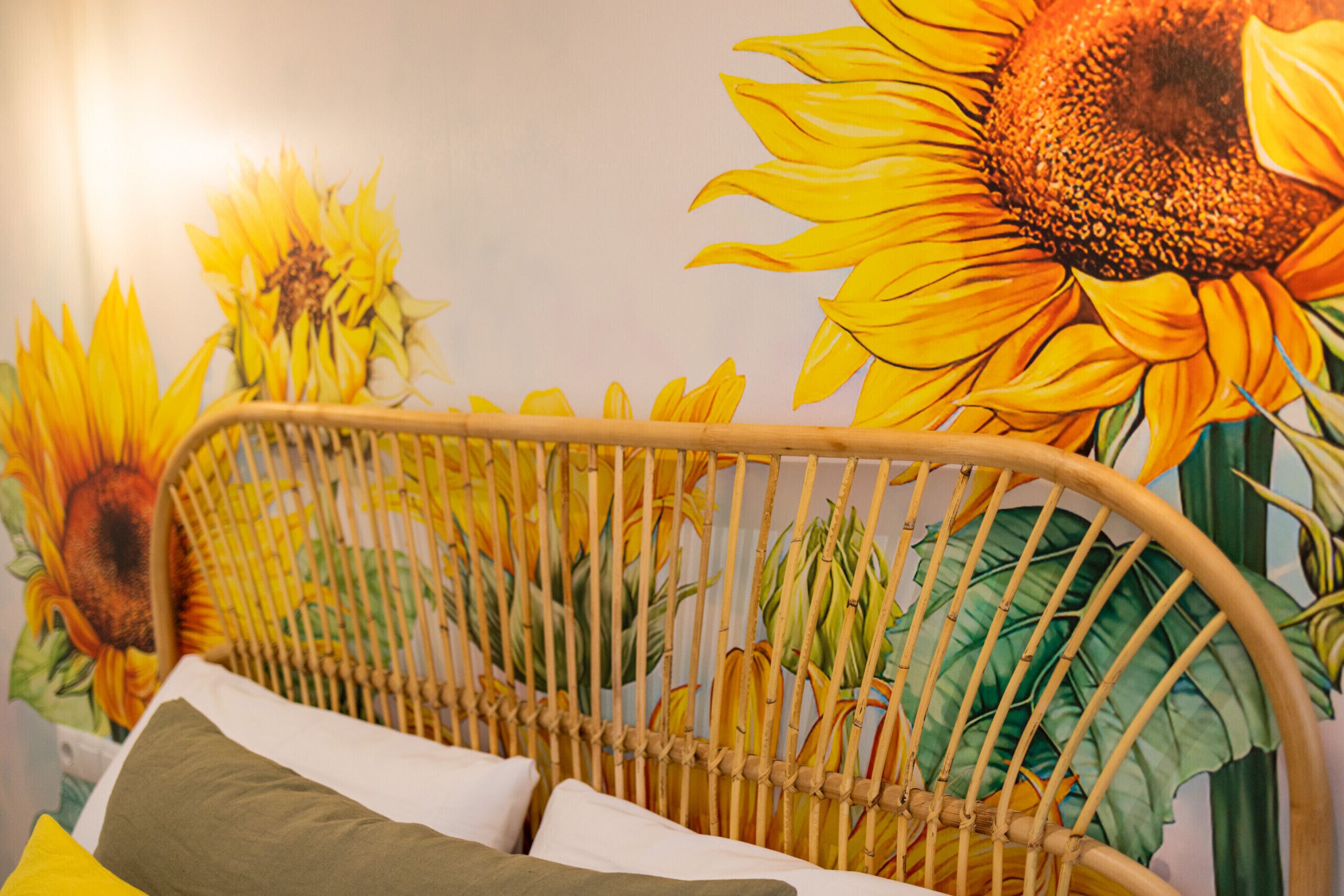 Una habitación con una cama, cabecero de mimbre y un mural de girasoles en la pared.