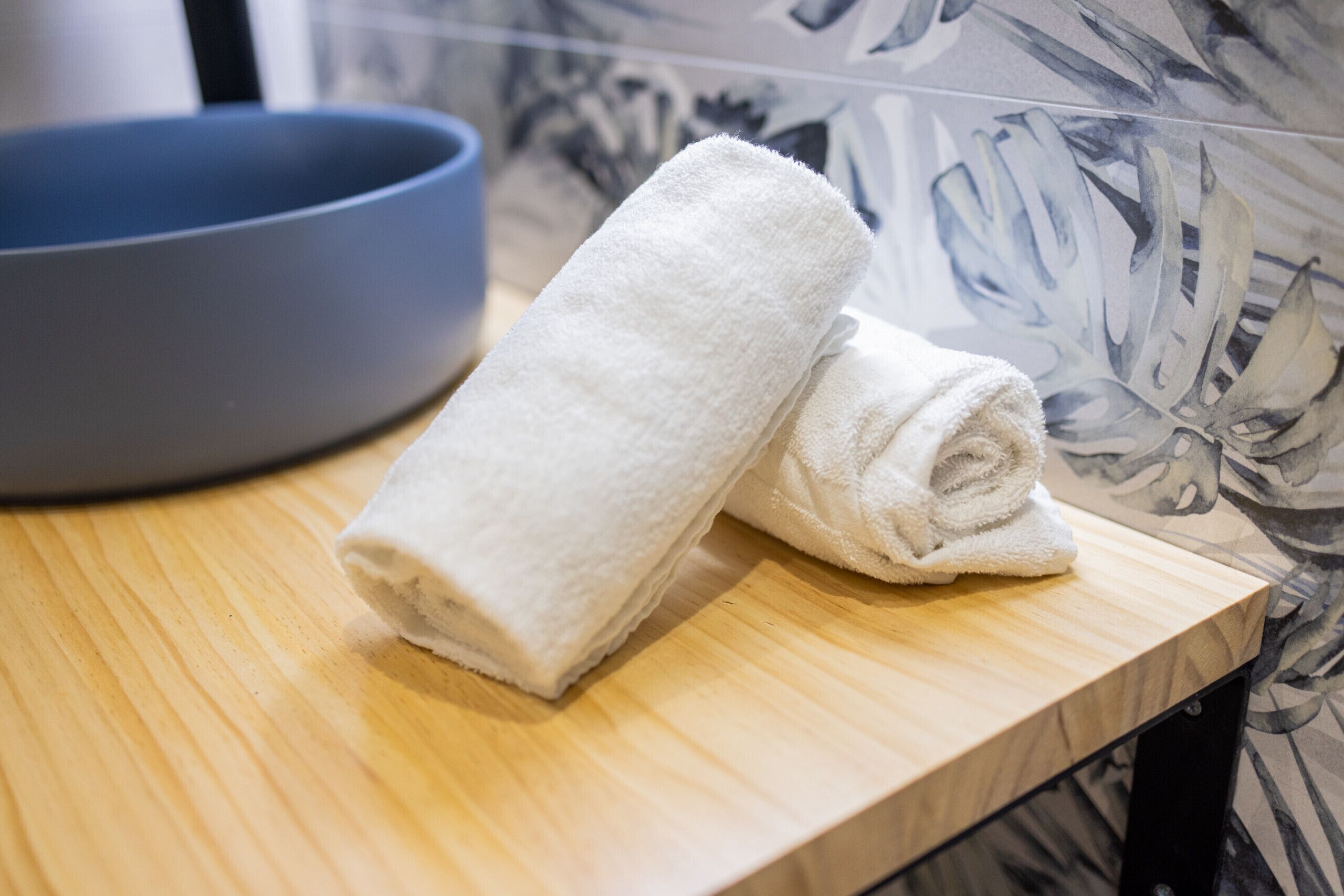 Een houten tafel met een opgerolde witte handdoek en een blauwe schaal.