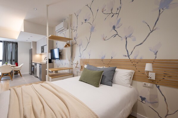 A modern hotel room with a large bed, a desk with a television, and a wall with a tree branch design.