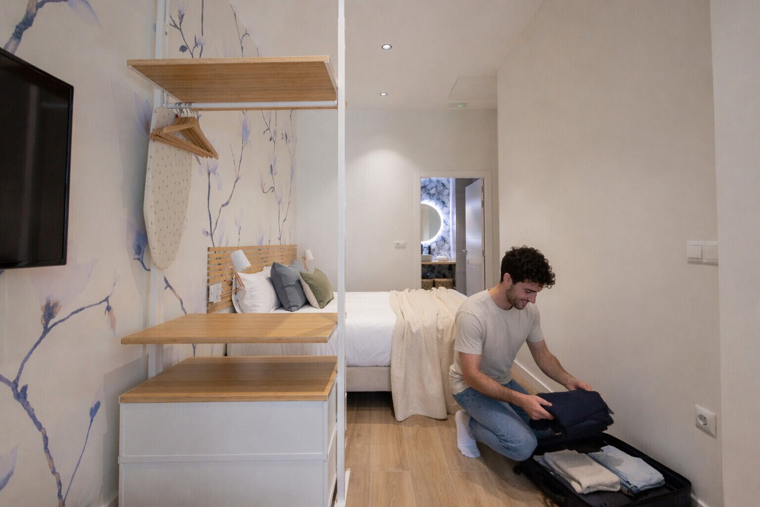 A bedroom with a bed, a wooden shelf unit, and a suitcase on the floor.