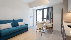 Un salon moderne avec un canapé bleu, une table à manger avec des chaises et un coin cuisine.