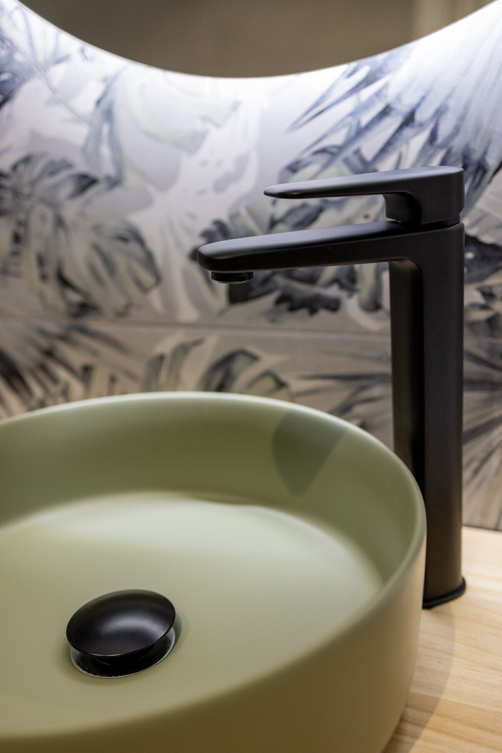 A modern bathroom with a green sink and a black faucet.