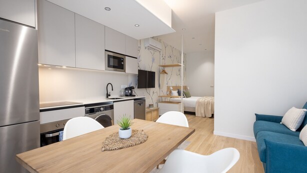 Une cuisine moderne dotée d’appareils électroménagers en acier inoxydable, un coin repas avec une table en bois, des chaises blanches et une petite plante en pot.