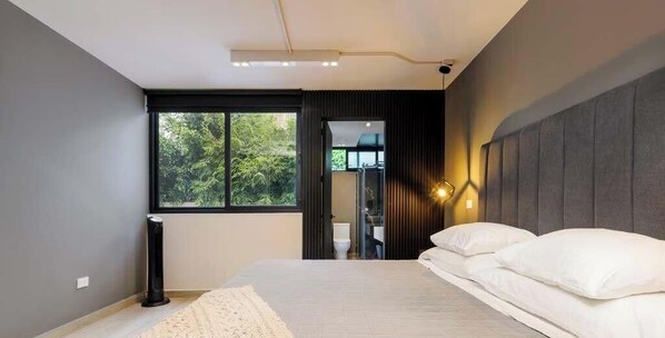 Une chambre moderne avec un grand lit, une table de chevet, une lampe sur pied et une fenêtre donnant sur un paysage verdoyant.