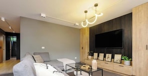 A modern living room with a grey sofa, a coffee table, and a flat-screen TV mounted on a wooden wall.