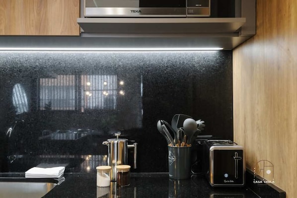 A modern kitchen with a black countertop, a coffee maker, a toaster, and a container with utensils.