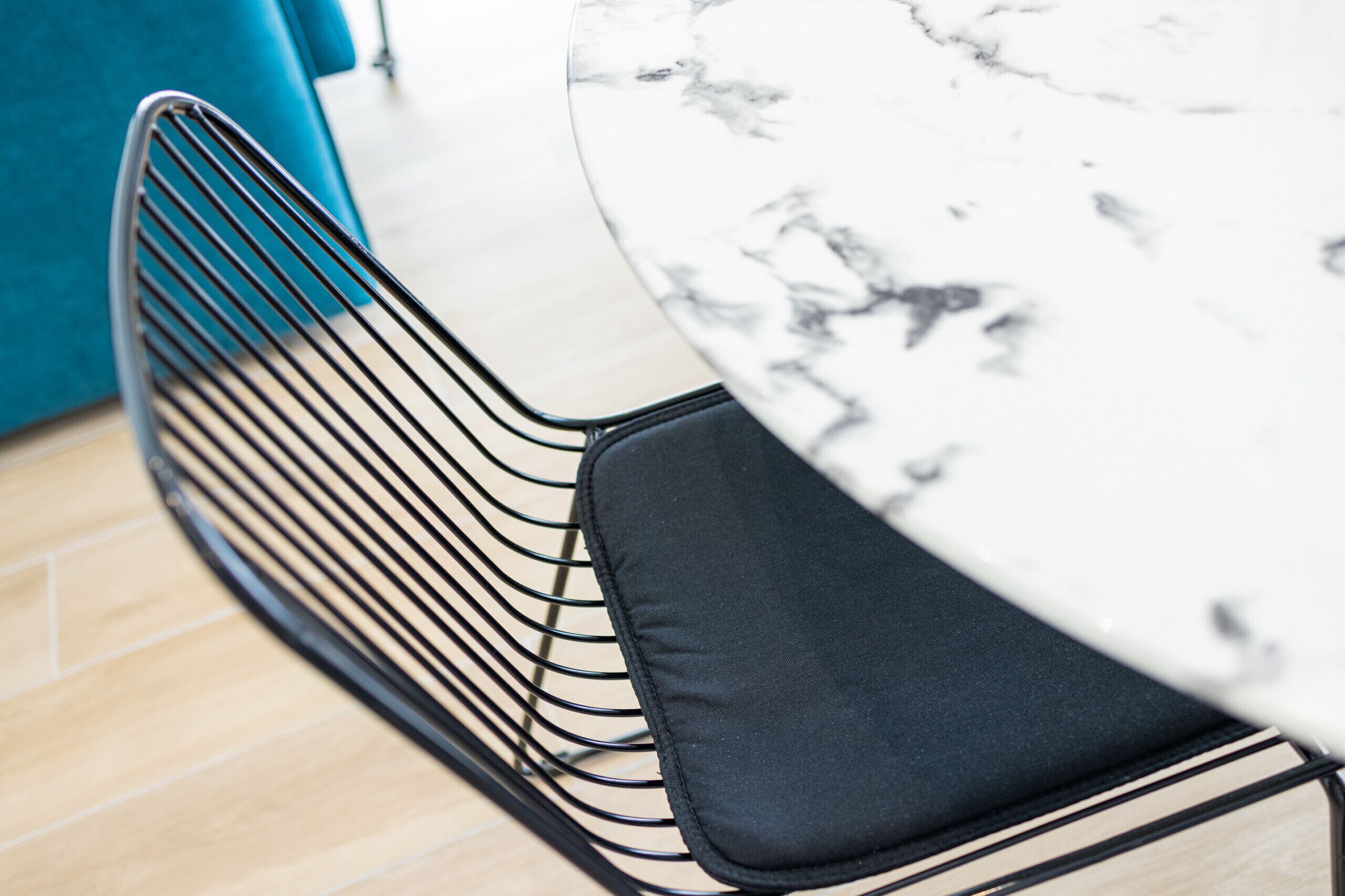Gros plan sur un coin repas moderne, avec une table ronde en marbre, une chaise en fil de fer noir et un mur de couleur turquoise.