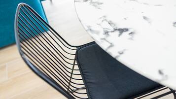 Gros plan sur un coin repas moderne, avec une table ronde en marbre, une chaise en fil de fer noir et un mur de couleur turquoise.