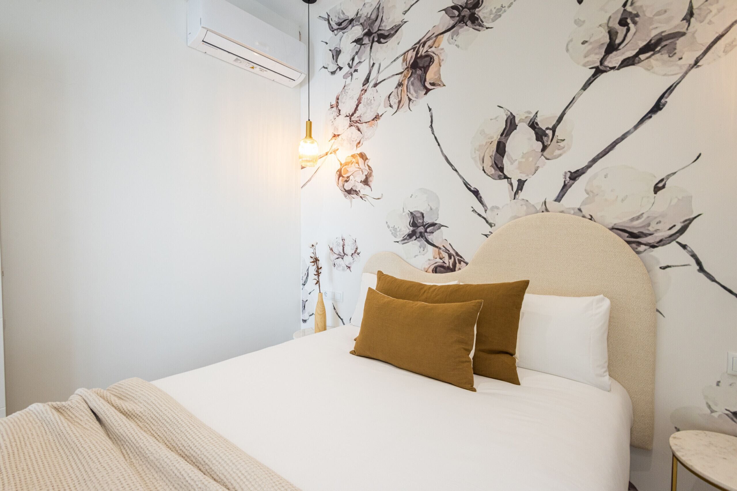 Un dormitorio con cama, cabecera, aire acondicionado de pared y pared con estampado floral.