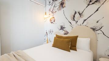 Un dormitorio con cama, cabecera, aire acondicionado de pared y pared con estampado floral.