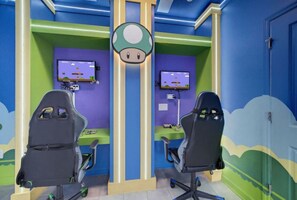 A gaming room with two gaming chairs, two monitors, and colorful wall art.