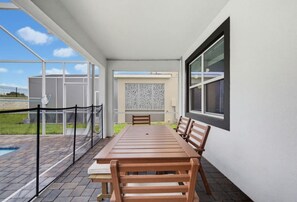 An outdoor patio with a long wooden table and chairs, a glass railing, and a view of a building in the background. - Super 8BR Resort Pool Vacation Home Near Disney (Davenport)