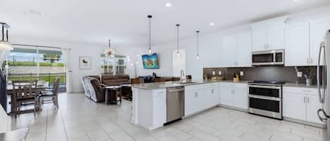 A modern kitchen with white cabinets, stainless steel appliances, and pendant lighting.