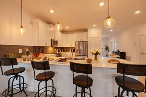 Una cocina moderna con armarios blancos, una isla central con taburetes y luminarias colgantes.