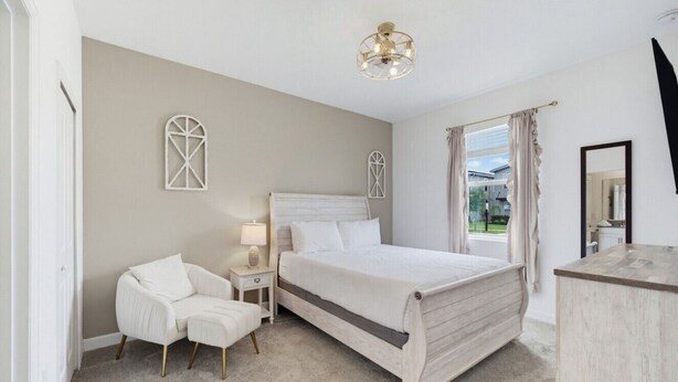 Een slaapkamer met een groot bed, een nachtkastje, een stoel en een raam met gordijnen.
