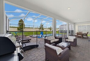 A covered patio area with outdoor furniture, a barbecue grill, and a view of a swimming pool and greenery. - Super 8BR Resort Pool Vacation Home Near Disney (Davenport)