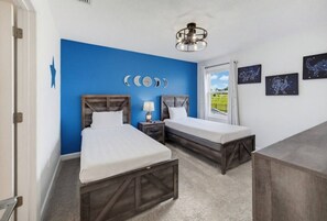 A bedroom with two beds, a nightstand, a lamp, and a window with a view.