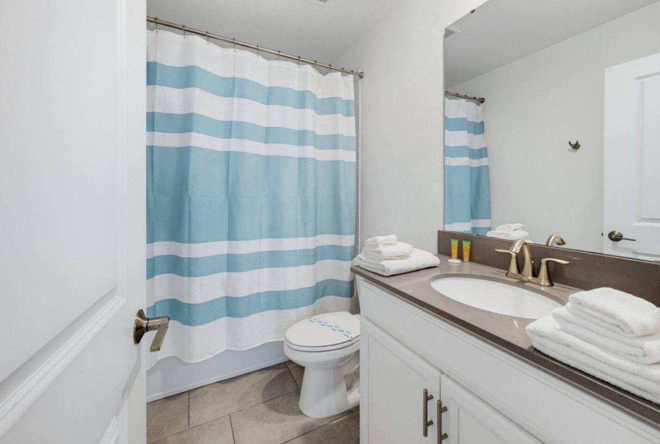 A bathroom with a striped shower curtain, a toilet, a sink with a mirror, and neatly folded towels.