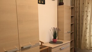 A modern room with a wooden wardrobe, a small desk with drawers, a world map on the wall, a potted plant, and a patterned rug.