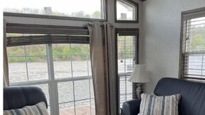 A room with a black leather sofa, a smaller armchair, and a lamp. Large windows provide a view of a body of water.