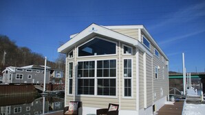 A waterfront house with a large bay window, a covered deck, and a dock.