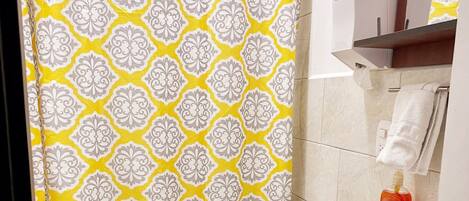 Un baño con cortina de ducha de diseño amarillo y blanco, un inodoro blanco, un lavabo blanco y un dispensador de jabón.