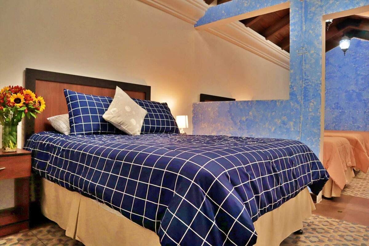 Un dormitorio con una cama grande, una mesita de noche, un jarrón con flores y una pared azul decorativa.