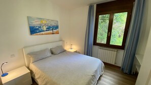 A bedroom with a bed, a nightstand, a painting, a window with curtains, and a radiator. - Blue Lake apartment with pool and lake view (Stresa)