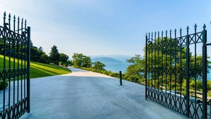 A paved pathway leading to a gated entrance with a view of a body of water and distant mountains. - Blue Lake apartment with pool and lake view (Stresa)