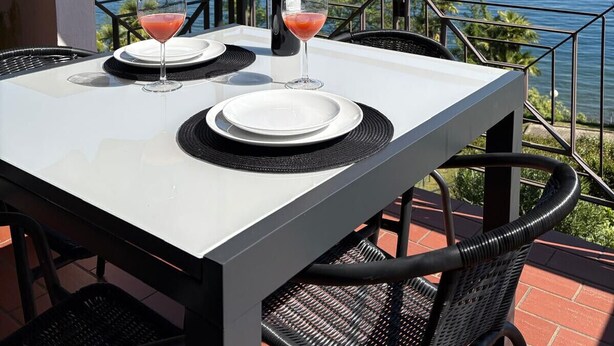A table with two wine glasses and a bottle, set on a balcony with a view of mountains and a lake. - Blue Lake apartment with pool and lake view (Stresa)