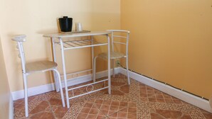 A corner room with a white metal shelf unit against a yellow wall, a white chair, and a tiled floor. - Economy Inn By OYO Lockport near Houma (Lockport)