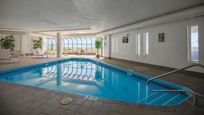 An indoor swimming pool with clear glass walls, lounge chairs, and potted plants. - Seawatch Oceanfront Unit 602 (Old Orchard Beach)