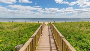 A wooden boardwalk leading to a beach with a clear view of the ocean and a grassy area. - Seawatch Oceanfront Unit 602 (Old Orchard Beach)