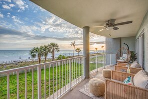 Un balcone con mobili in vimini, una ventola a soffitto e vista sulla spiaggia e sull'oceano.