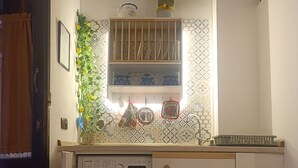 Ett kompakt kök med tvättmaskin, en liten hylla med dekorativa föremål och ett mönstrat stänkskydd.