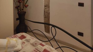 Ett sovrum med en säng, ett fönster med gardin, en vägg med en synlig tegelstenssektion och en liten växt på nattduksbordet.