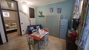 Ett kompakt bostadsutrymme med ett matbord, stolar, en soffa, en säng, en garderob och ett litet kylskåp.