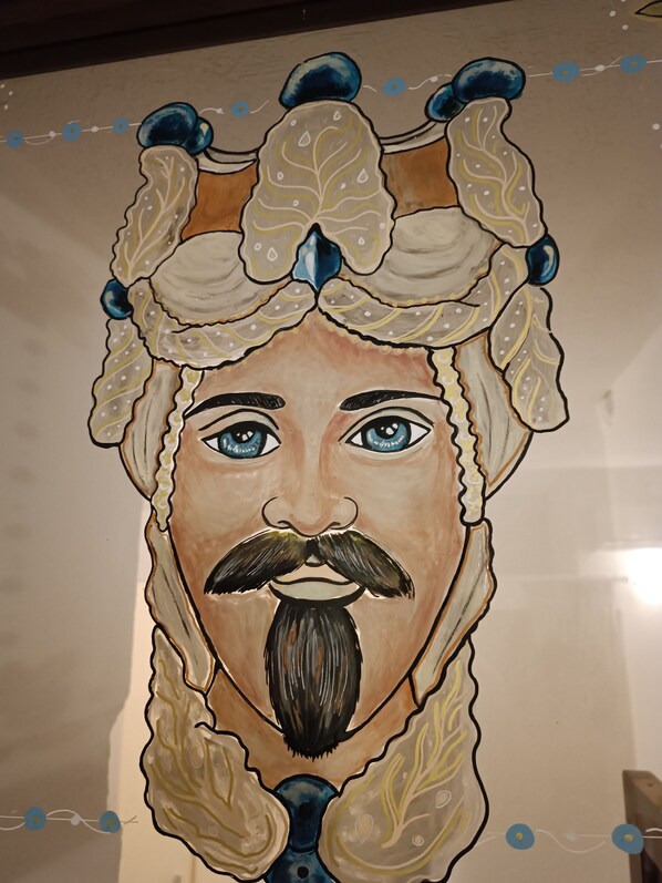 Portret van een persoon met een snor en baard, die een decoratieve hoofdtoots met blauwe en witte accenten draagt.