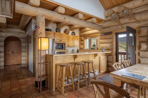 A log cabin interior with a kitchen, bar stools, a dining table, and a large window. - Windance Cabin, Private Beach on 750 Acres For You (Garfield County)