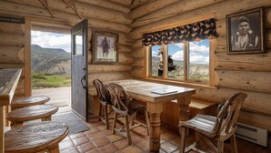 A log cabin interior with a wooden dining table, chairs, a window with a view of the landscape, and framed pictures on the walls. - Windance Cabin, Private Beach on 750 Acres For You (Garfield County)