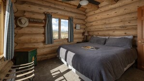 A log cabin bedroom with a bed, a ceiling fan, a window with curtains, and a sign on the wall. - Windance Cabin, Private Beach on 750 Acres For You (Garfield County)