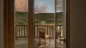 A wooden deck with two rocking chairs overlooking a landscape with a dirt path and grassy hills. - Windance Cabin, Private Beach on 750 Acres For You (Garfield County)