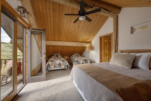 A bedroom with a large bed, two smaller beds, a ceiling fan, and a view through a glass door.
