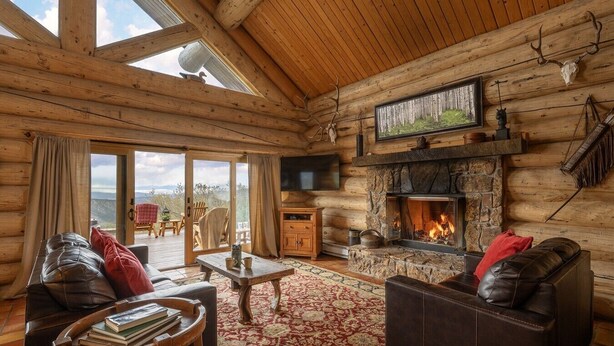 A log cabin interior with a fireplace, leather sofas, a television, and a view through the glass door. - Windance Cabin, Private Beach on 750 Acres For You (Garfield County)