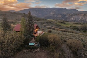 A cabin with a red roof, a hot tub, and a deck overlooking a mountainous landscape. - Windance Cabin, Private Beach on 750 Acres For You (Garfield County)